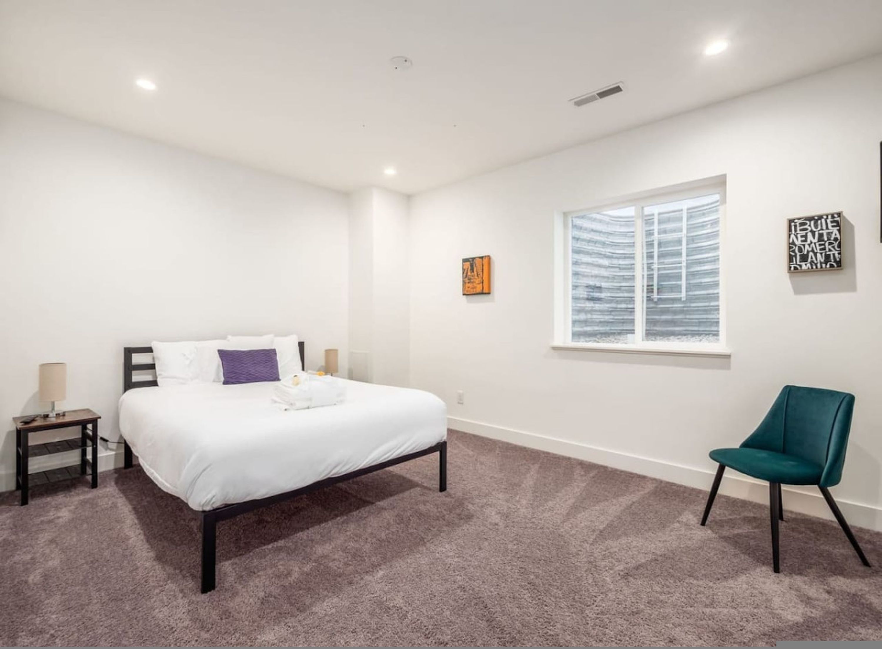 Une chambre à coucher avec un lit, une chaise, une fenêtre et des œuvres d’art accrochées au mur.