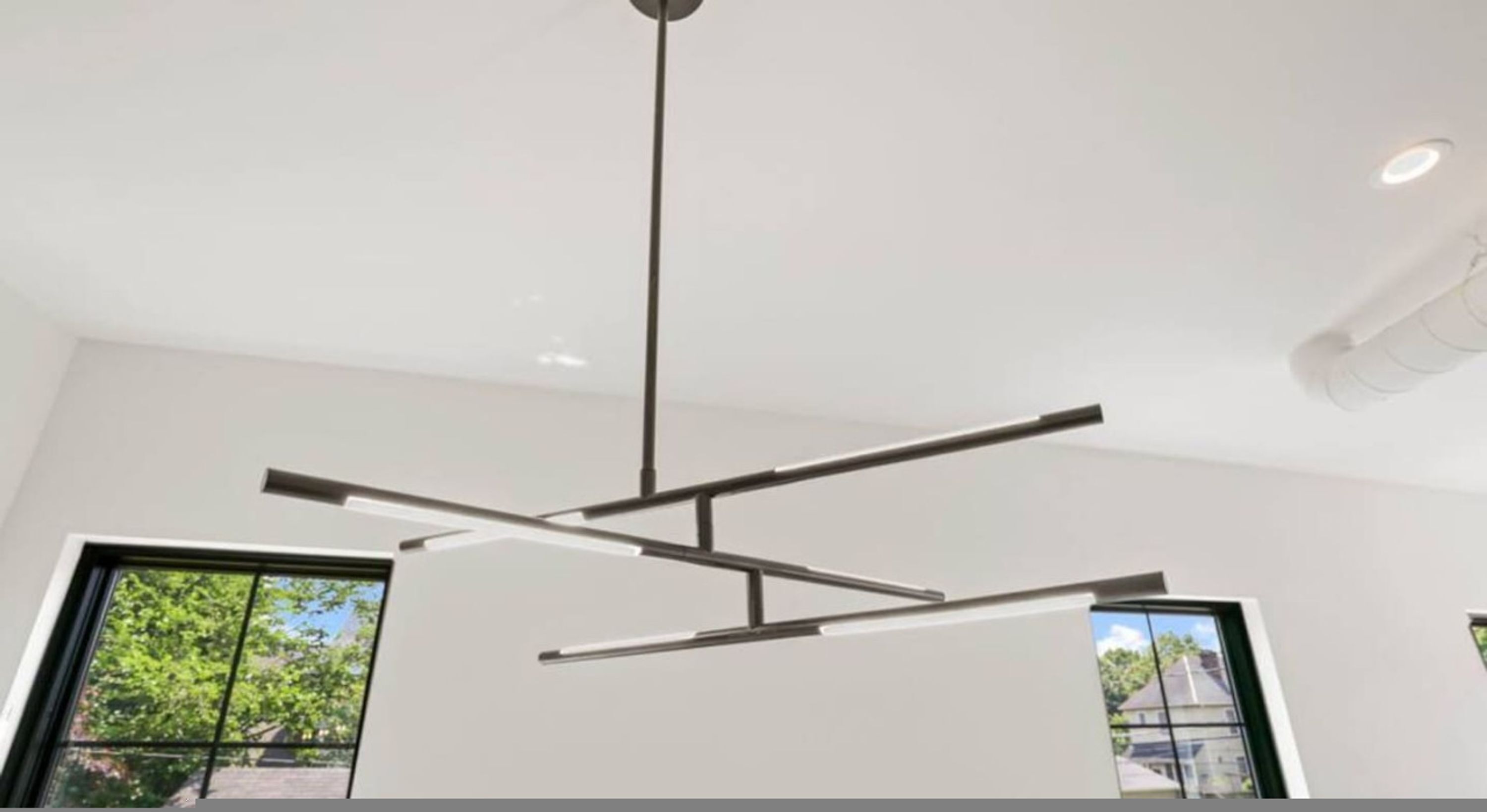A modern interior with a minimalist ceiling design, large windows, and a view of greenery outside.