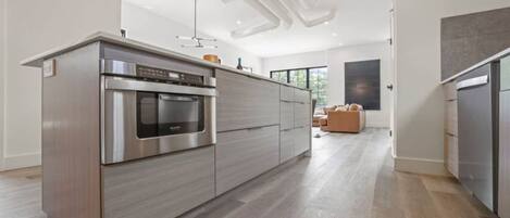 A modern kitchen with a built-in oven and microwave, wooden cabinets, and a light-colored floor.
