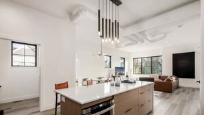 Une cuisine moderne dotée d’un îlot central, d’un four encastré et de luminaires suspendus.