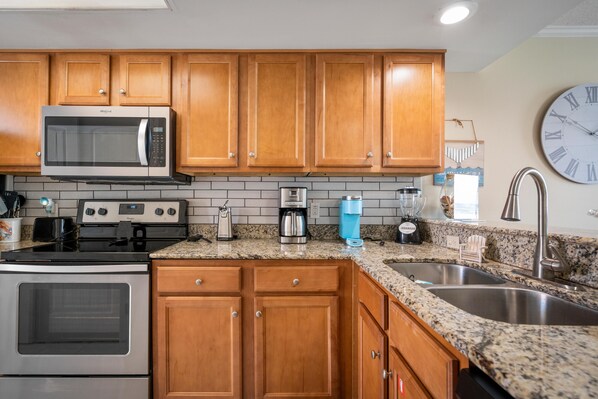 A kitchen with wooden cabinets, a stainless steel microwave, a stove, a coffee maker, and a sink. - The Whaler B6 (Gulf Shores)