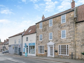 Un bâtiment en pierre avec une porte blanche portant l’inscription « Warrington », une enseigne indiquant « Artisan Frames », et une vue de la rue avec une voiture garée.