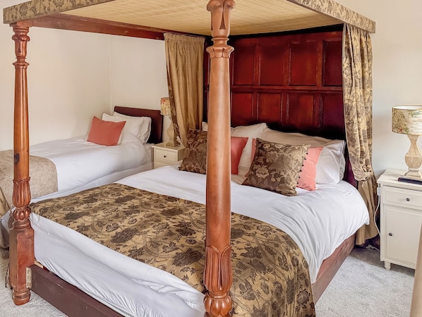 Un lit à baldaquin à quatre poteaux avec une structure en bois, deux tables de chevet et une petite table de nuit avec une lampe.