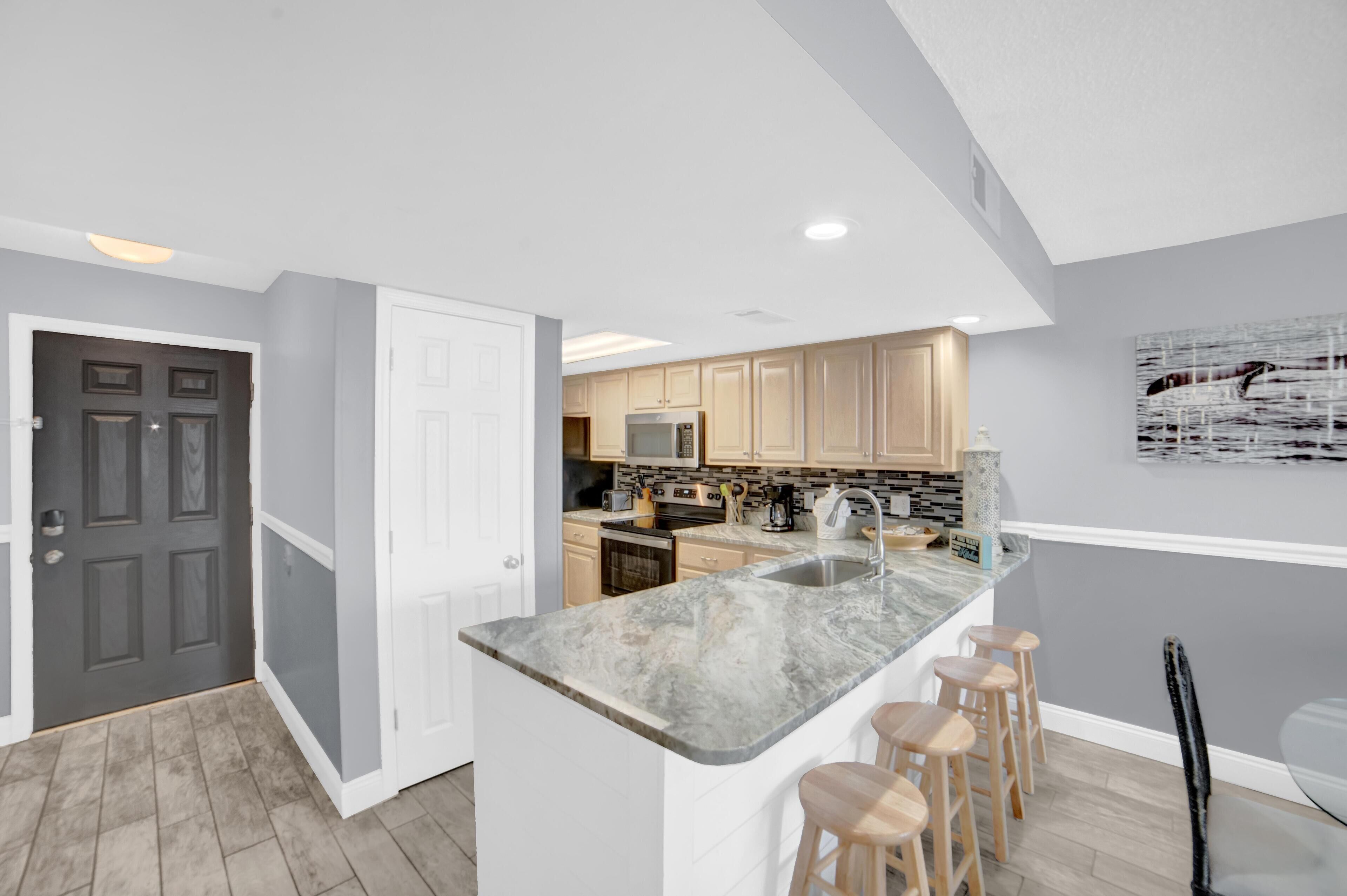 A modern kitchen with a marble island, wooden stools, and light-colored cabinets.