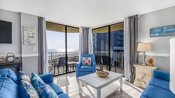 A balcony with a view of the sea, furnished with blue sofas, a table, and a chair. - The Whaler B3 (Gulf Shores)