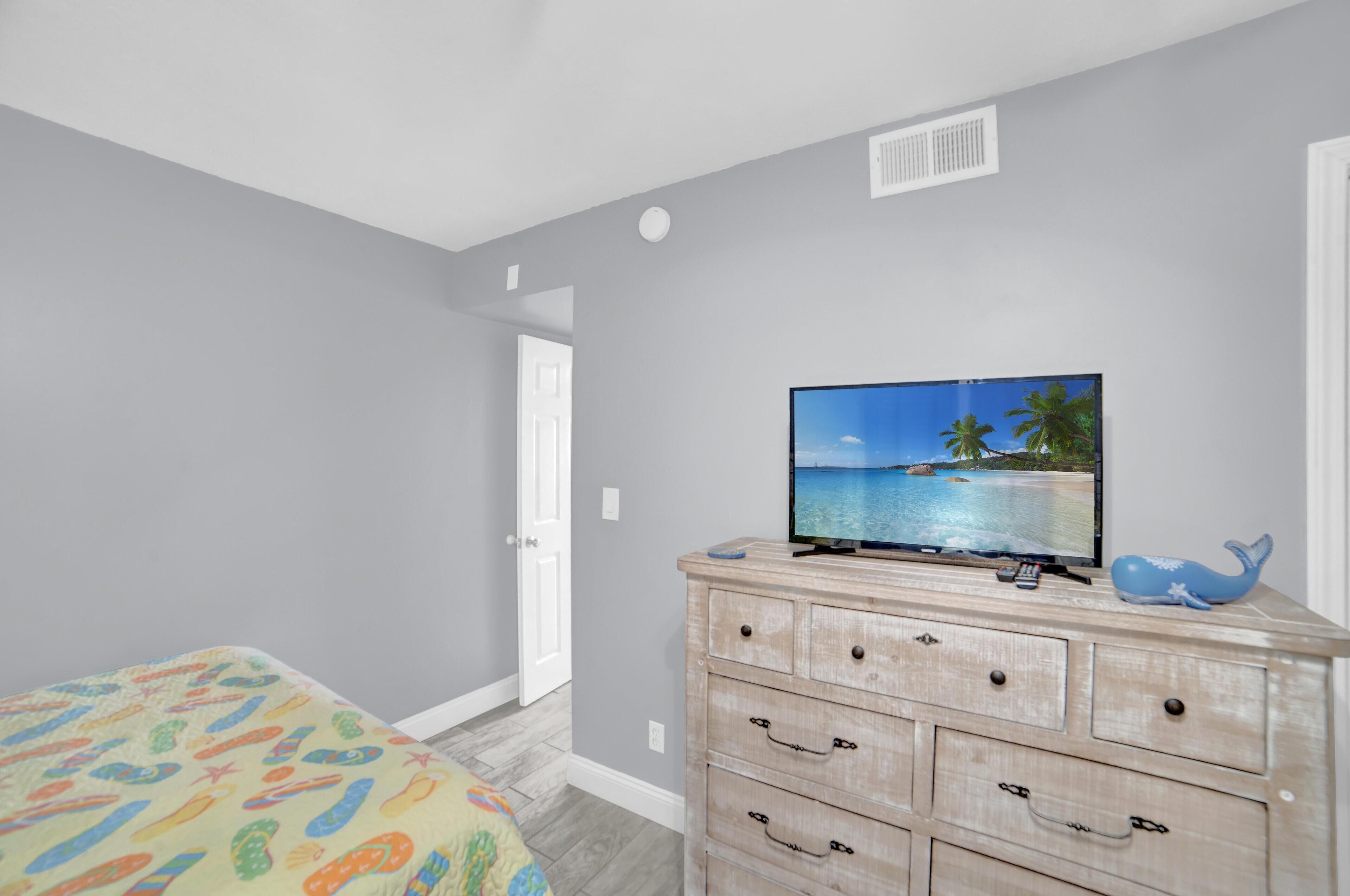 A bedroom with a bed, a dresser, and a television displaying a beach scene.