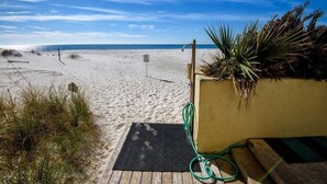 A beach with a wooden deck, a green hose, and a palm plant. - The Whaler B3 (Gulf Shores)