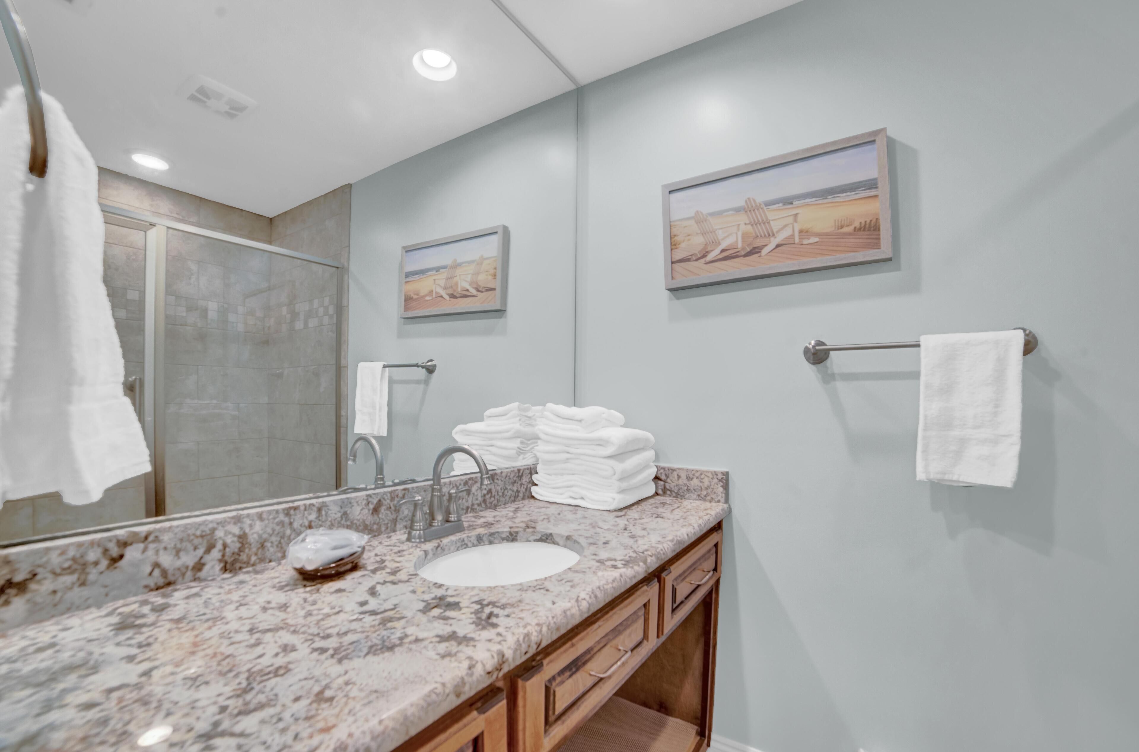 Un baño con lavabo de mármol, cabina de ducha de cristal y dos cuadros en la pared.