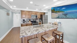 A modern kitchen with wooden cabinets, stainless steel appliances, and a large island with bar stools. - Sugar Beach 348 (Orange Beach)