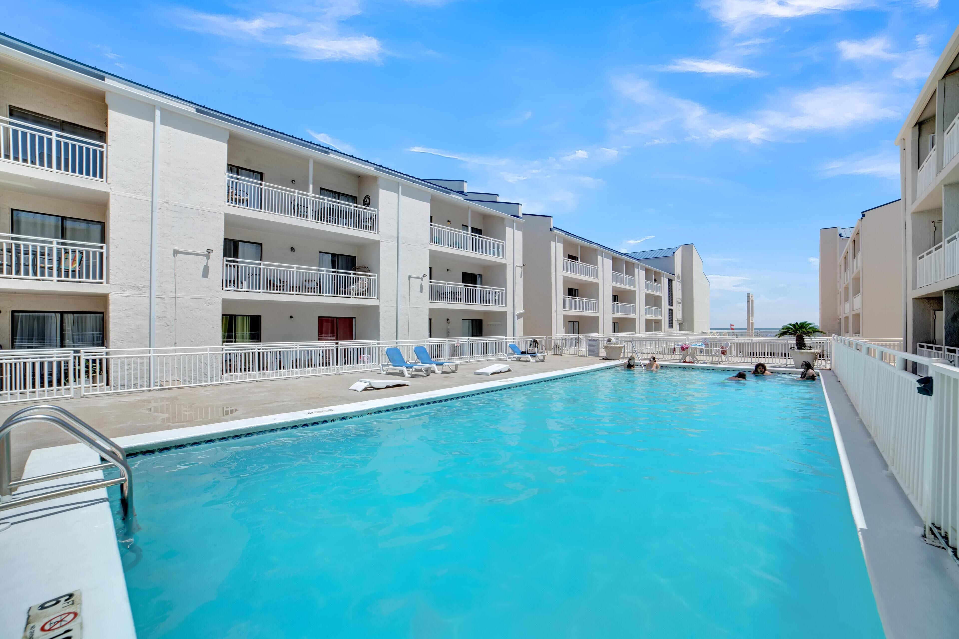 Piscina com espreguiçadeiras e um prédio com varandas.
