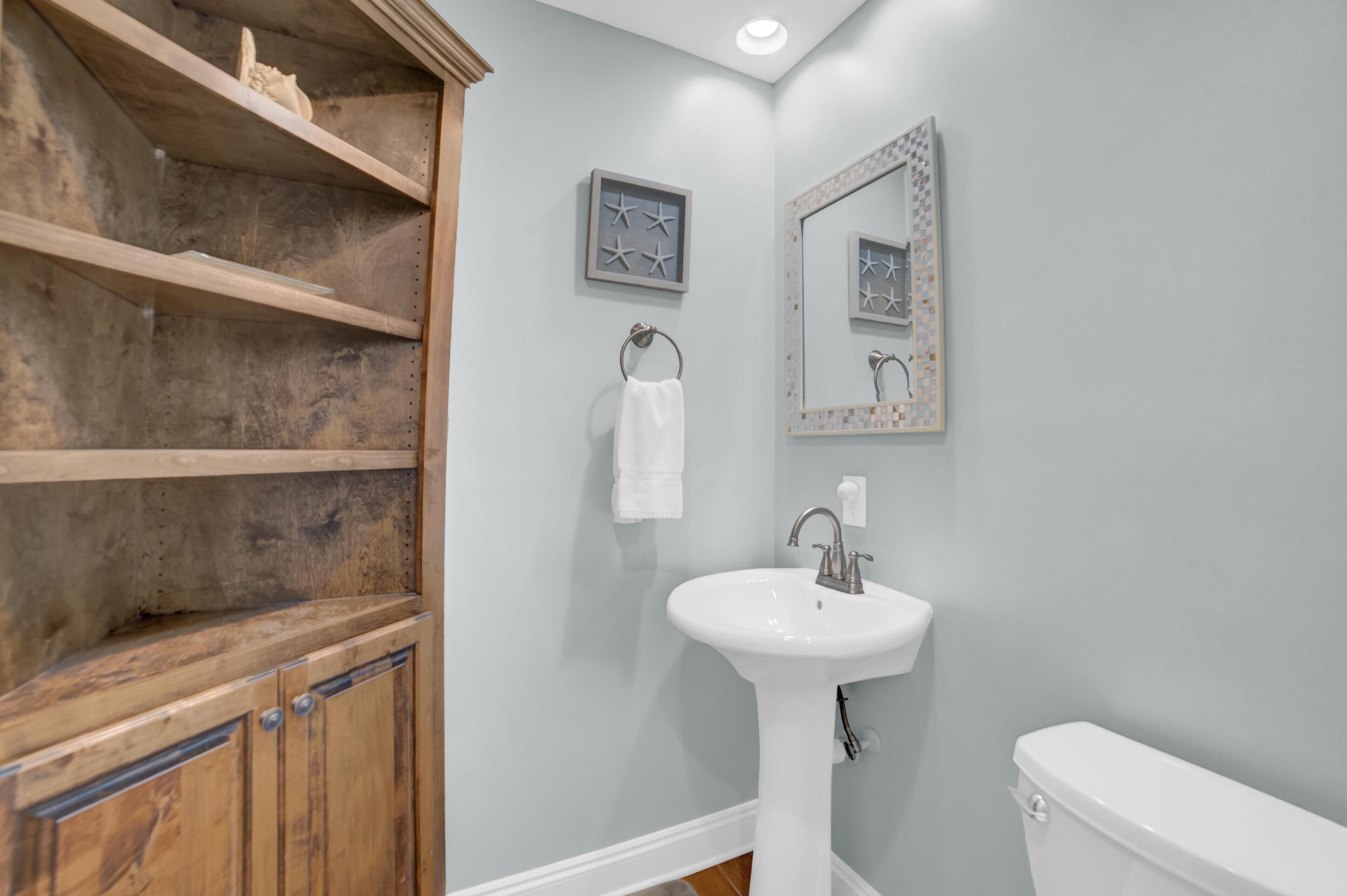 A bathroom with a wooden vanity, a white sink, a toilet, a towel rack, and a mirror with a decorative frame.