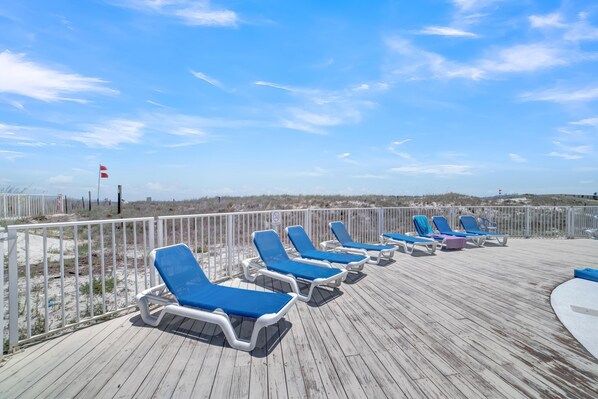 A wooden deck with blue lounge chairs and a white railing. - Sugar Beach 352 (Orange Beach)
