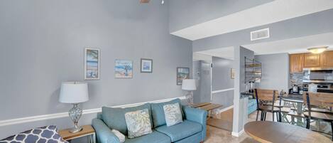 Un salon avec un canapé bleu, une table à manger en bois et un ventilateur de plafond.