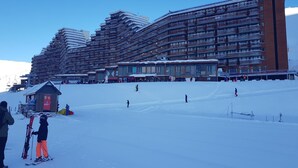 A ski resort with multiple buildings, including a large hotel with balconies and a smaller structure with a red sign. - Rental La Mongie Tourmalet at the foot of the slopes studio sleeps 5 (Bagnères-de-Bigorre)