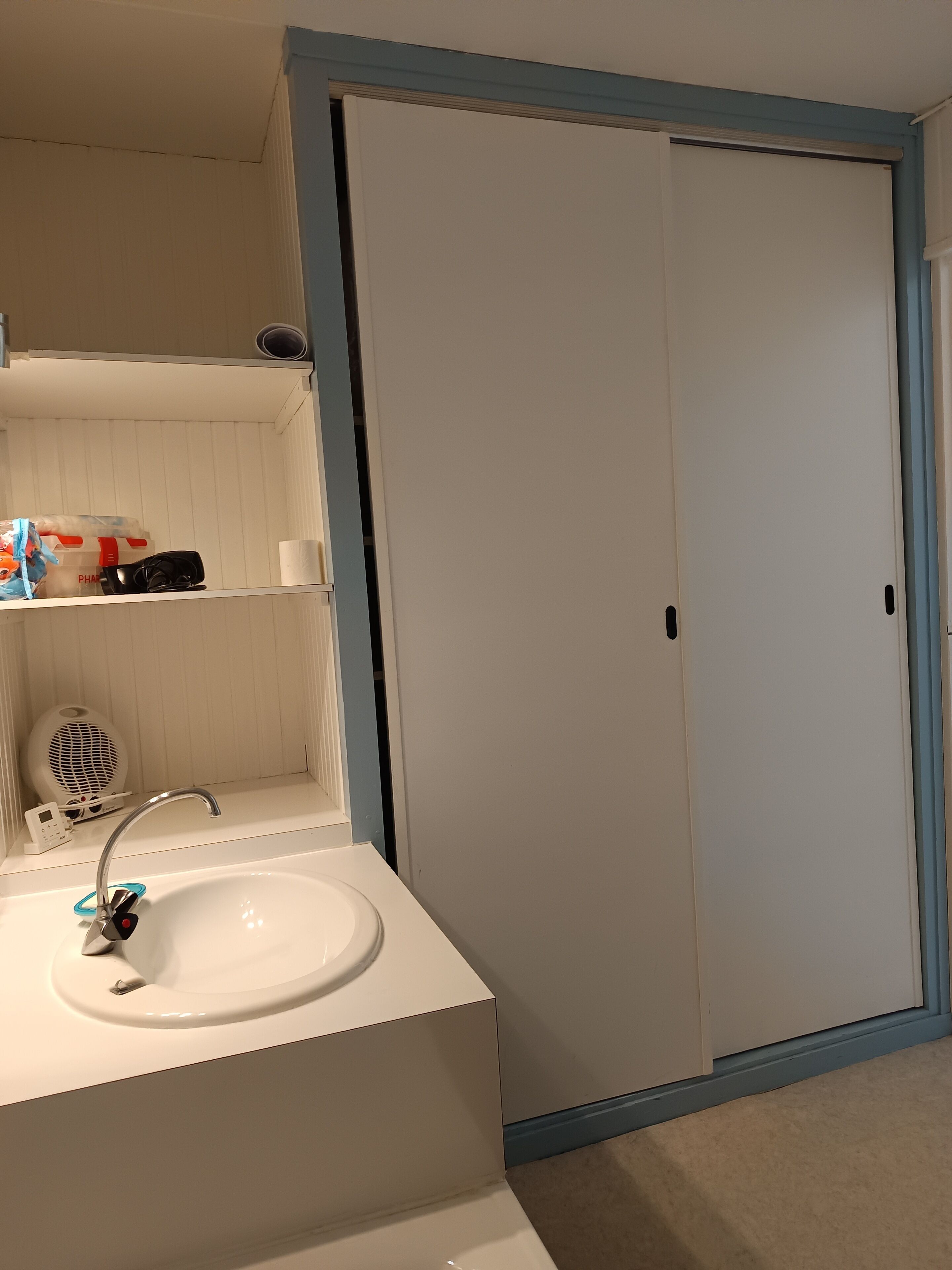 Bagno con lavandino bianco, uno specchio, un portascopevoli e una porta con cornice blu.