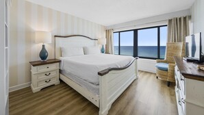 Quarto de hotel com cama, mesas de cabeceira, televisão e vista para o mar.