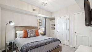 A bedroom with a bed, bedside lamp, wardrobe, and a TV mounted on the wall. - Battleship Vista - Parking (Wilmington)