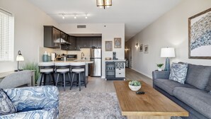 A modern living room with a sofa, a coffee table, and a kitchen area with bar stools. - Battleship Vista - Parking (Wilmington)