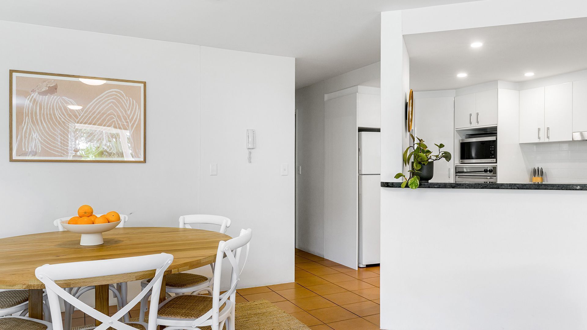 Une cuisine moderne avec des armoires blanches, un comptoir noir et des appareils en acier inoxydable. On y trouve également un coin repas avec une table en bois et des chaises blanches.