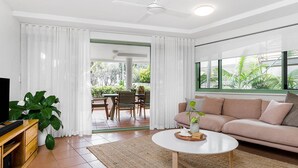 A modern living room with a sofa, coffee table, and TV stand. There is a dining area with chairs and a table visible through the doorway. - Apartment 2 Surfside. Combining an amazing beachside location, just 500m from town (Byron Bay)