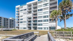 Un hôtel à plusieurs étages doté de balcons, d’une terrasse en bois et de palmiers.