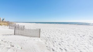 Une plage de sable bordée d’une clôture en bois, sous un ciel bleu et dégagé.