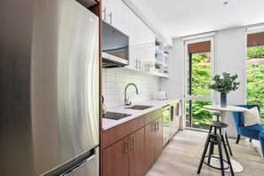 A modern kitchen with stainless steel appliances, white cabinetry, and a large window offering a view of greenery.