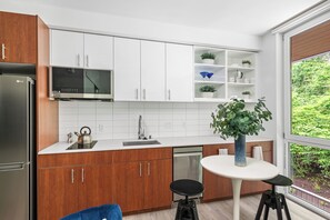 Une cuisine moderne avec des meubles blancs, un four à micro-ondes encastré, une bouilloire et un coin repas comprenant une table et des tabourets.