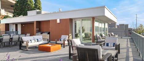 Eine Dachterrasse mit Sitzgelegenheiten im Freien, einem Grillbereich und einem gläsernen Raum.