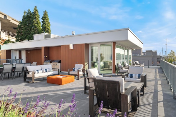 A rooftop terrace with outdoor seating, a barbecue area, and a glass-enclosed space.