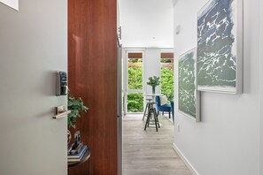 A hallway with a wooden door, a view of a patio with a table and chairs, and a wall with a framed artwork.