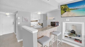 A modern kitchen with a marble countertop, white cabinetry, and a large island with bar stools. - Sugar Beach 356 (Orange Beach)