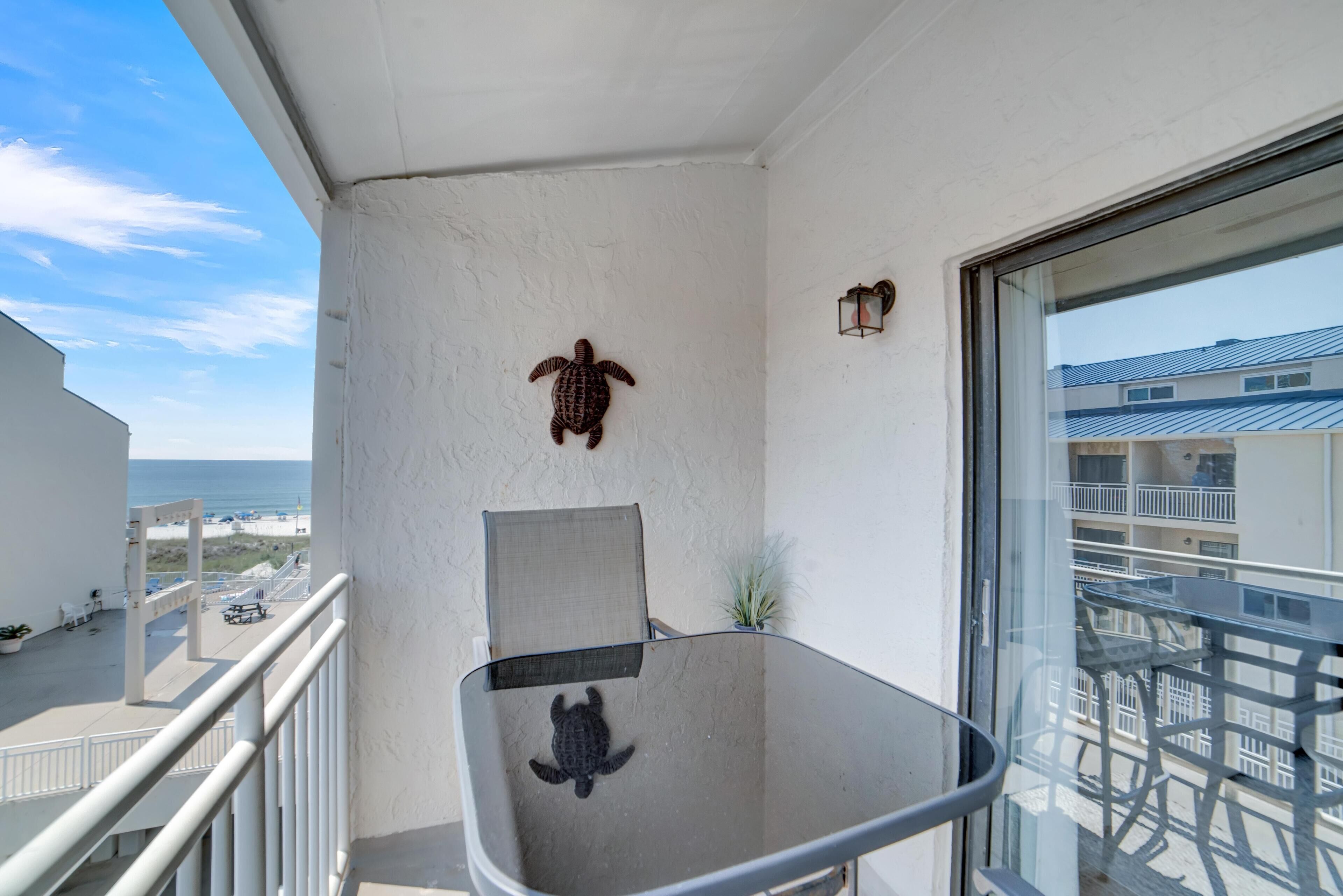 Un balcon avec une table en verre, une chaise, un pot de fleurs et une décoration murale représentant une tortue.