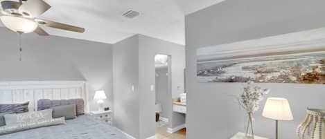 Ein Schlafzimmer mit einem Bett, Nachttischen, einem Deckenventilator, einem Gemälde und einer Vase mit Blumen.