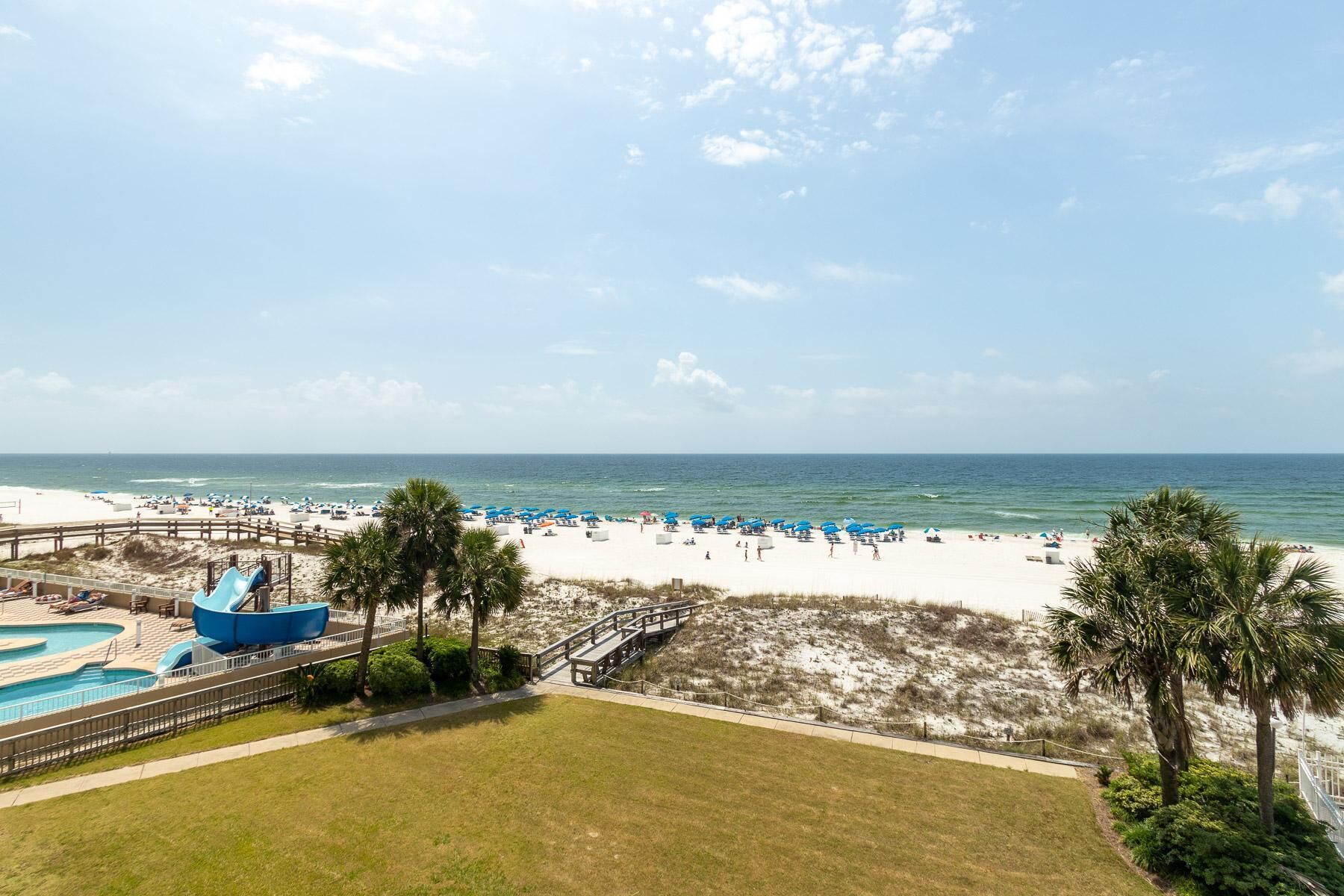 A beach resort with a pool area, beach umbrellas, and a boardwalk leading to the beach.