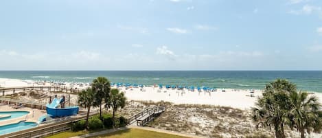A beach resort with a pool area, beach umbrellas, and a boardwalk leading to the beach.