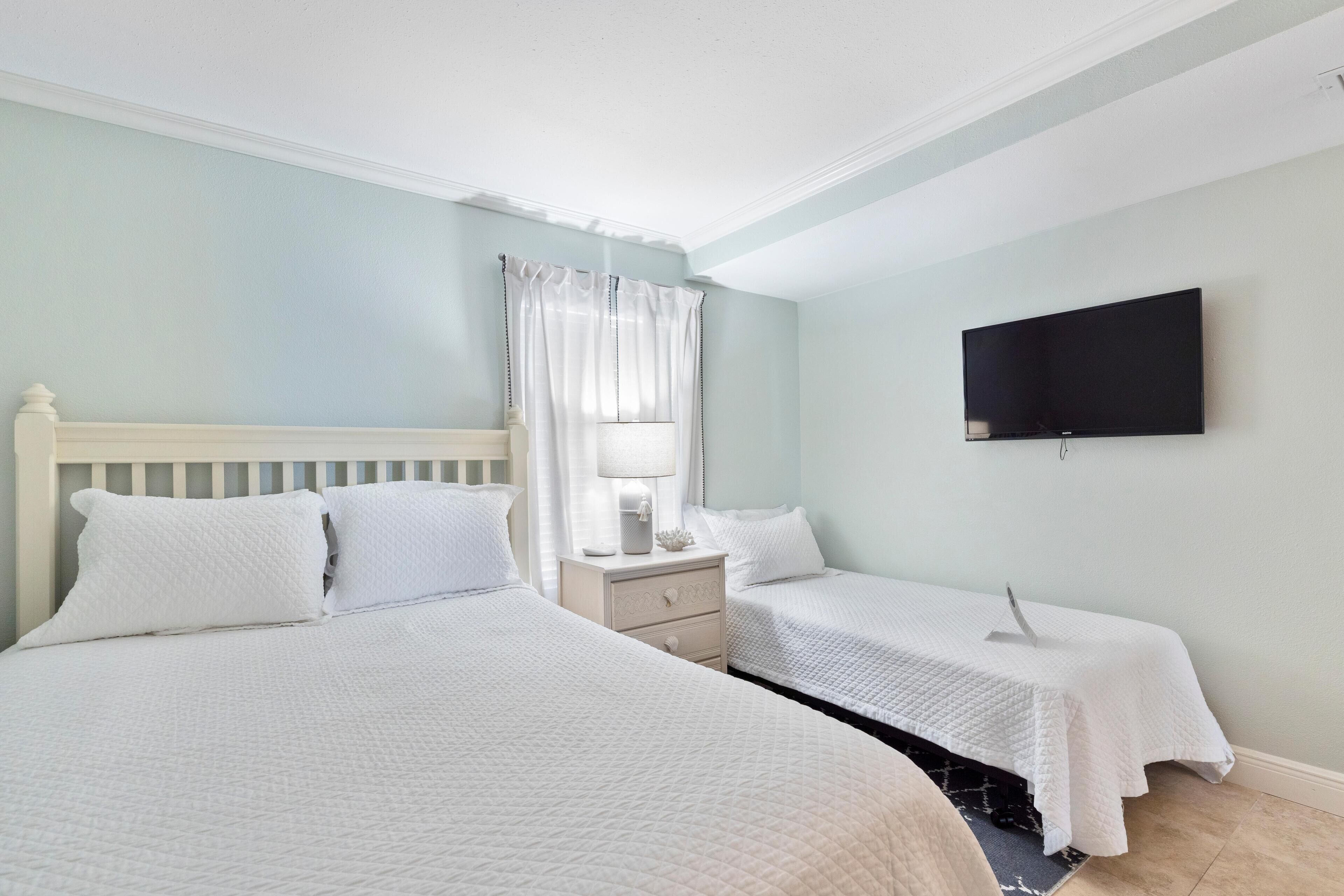 A hotel room with two beds, a TV, a nightstand, and a window with curtains.