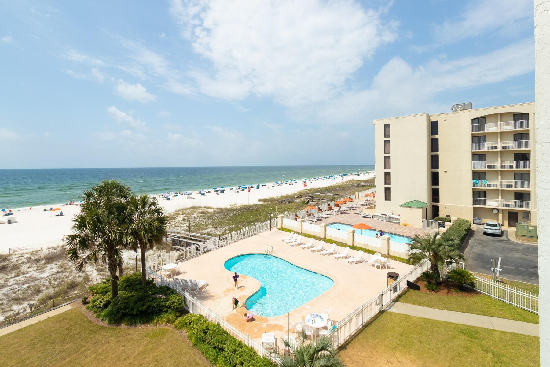 A hotel with a pool area, beach view, and a parking lot.