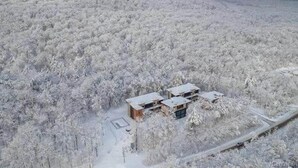 A remote, snow-covered landscape with a small cluster of buildings, likely a cabin or lodge, surrounded by dense forest.