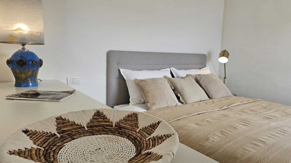 A bedroom with a grey headboard, multiple pillows, a bedside lamp, and a decorative woven basket.