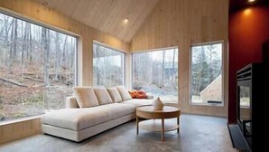 A modern interior with a sectional sofa, a round coffee table, and large windows offering a view of a wooded area.