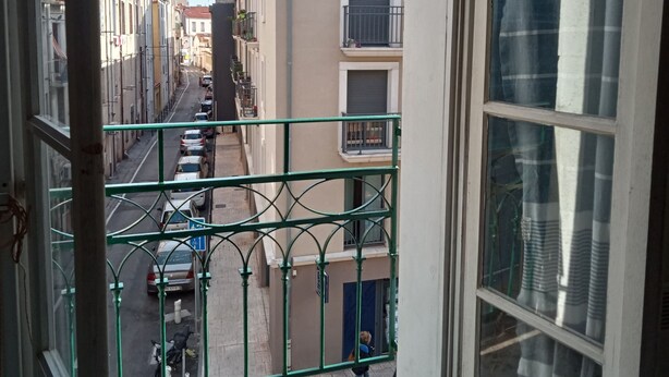 Rua estreita com edifícios de ambos os lados, uma faixa de pedestres e uma pessoa caminhando.