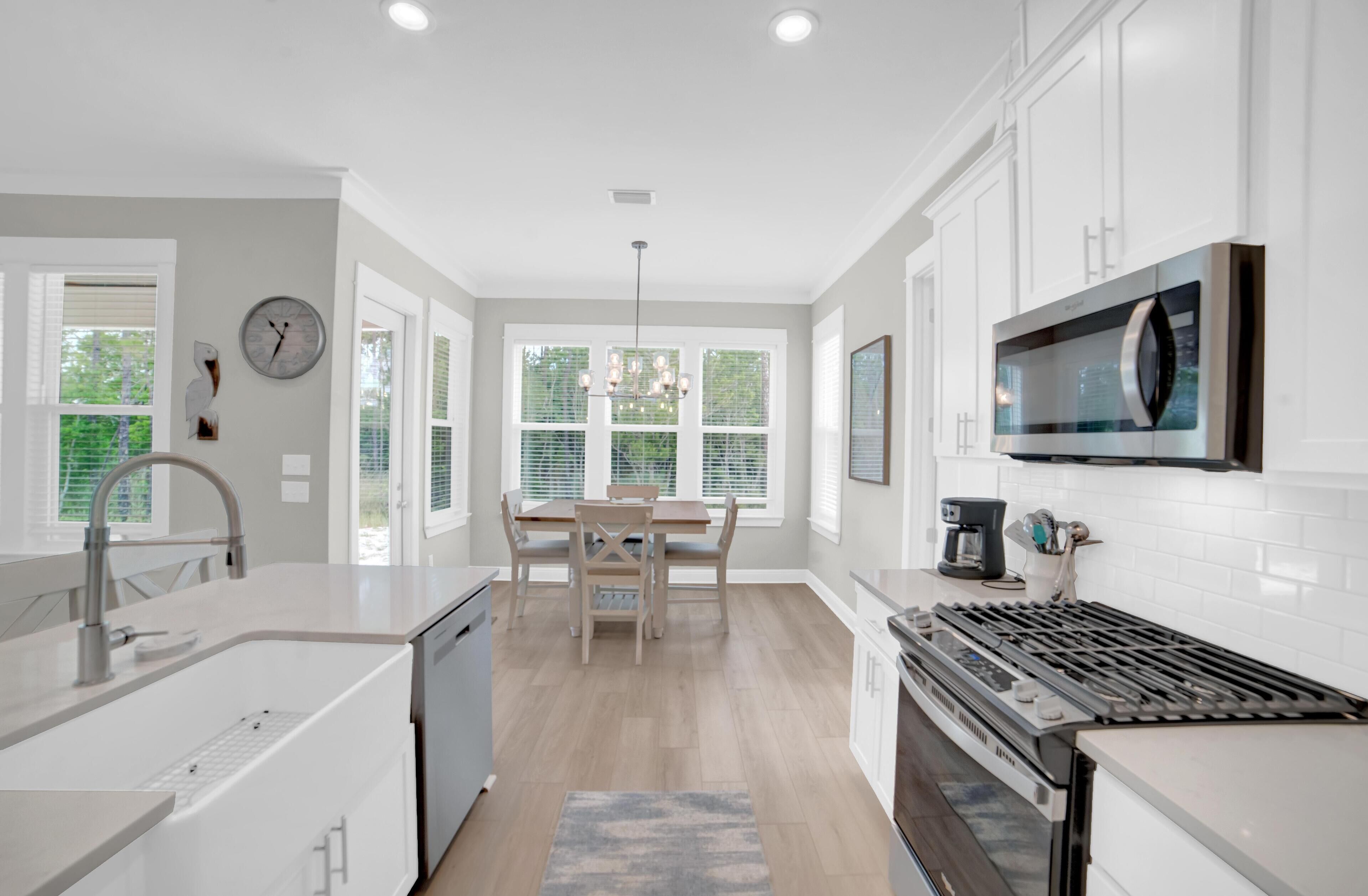 A modern kitchen with white cabinetry, a built-in stove, and a dining area with a table and chairs.