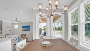 A dining area with a wooden table, white chairs, and a chandelier. - Summer Salt 24181 (Orange Beach)