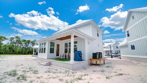 A white beach house with a covered porch, a small table, and a covered grill. - Summer Salt 24181 (Orange Beach)