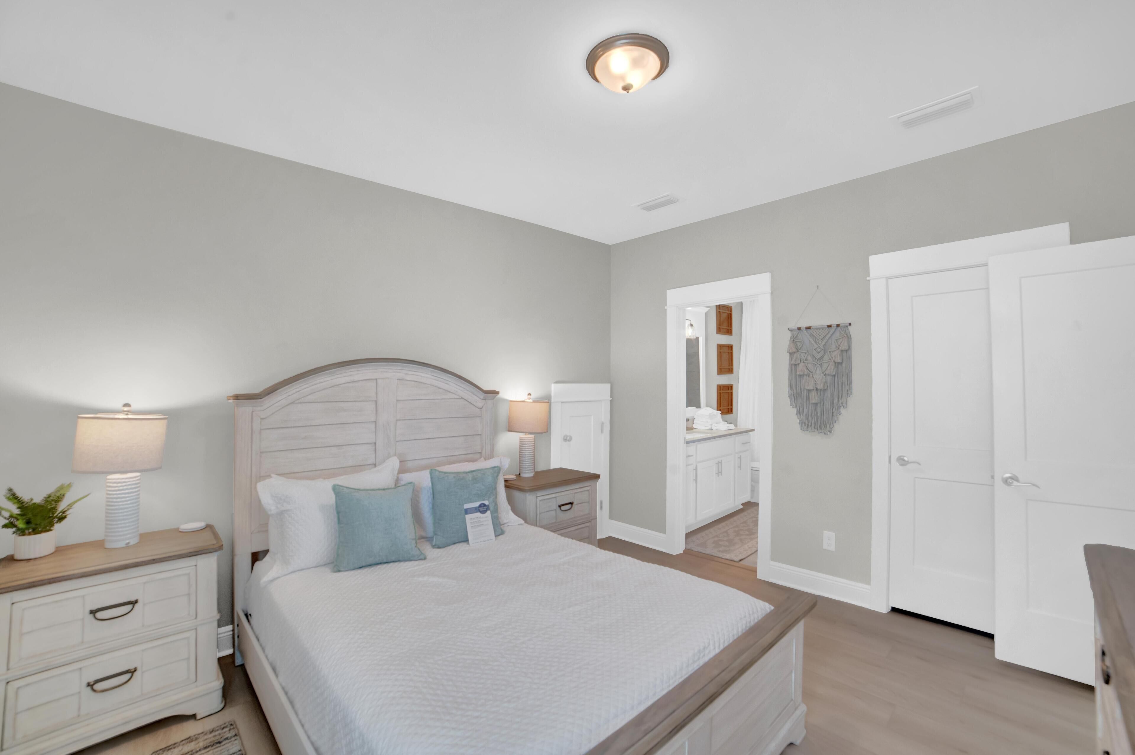 A bedroom with a bed, nightstands, a dresser, and a bathroom with a mirror and cabinets.