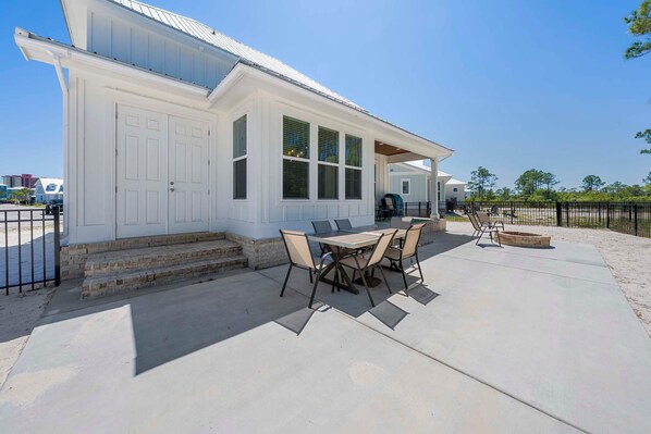 A house with a covered patio, a dining table with chairs, and a fire pit.