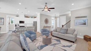 A spacious living area with a sofa, armchairs, and a coffee table. There is a kitchen in the background with white cabinets and a ceiling fan. - Summer Salt 24181 (Orange Beach)