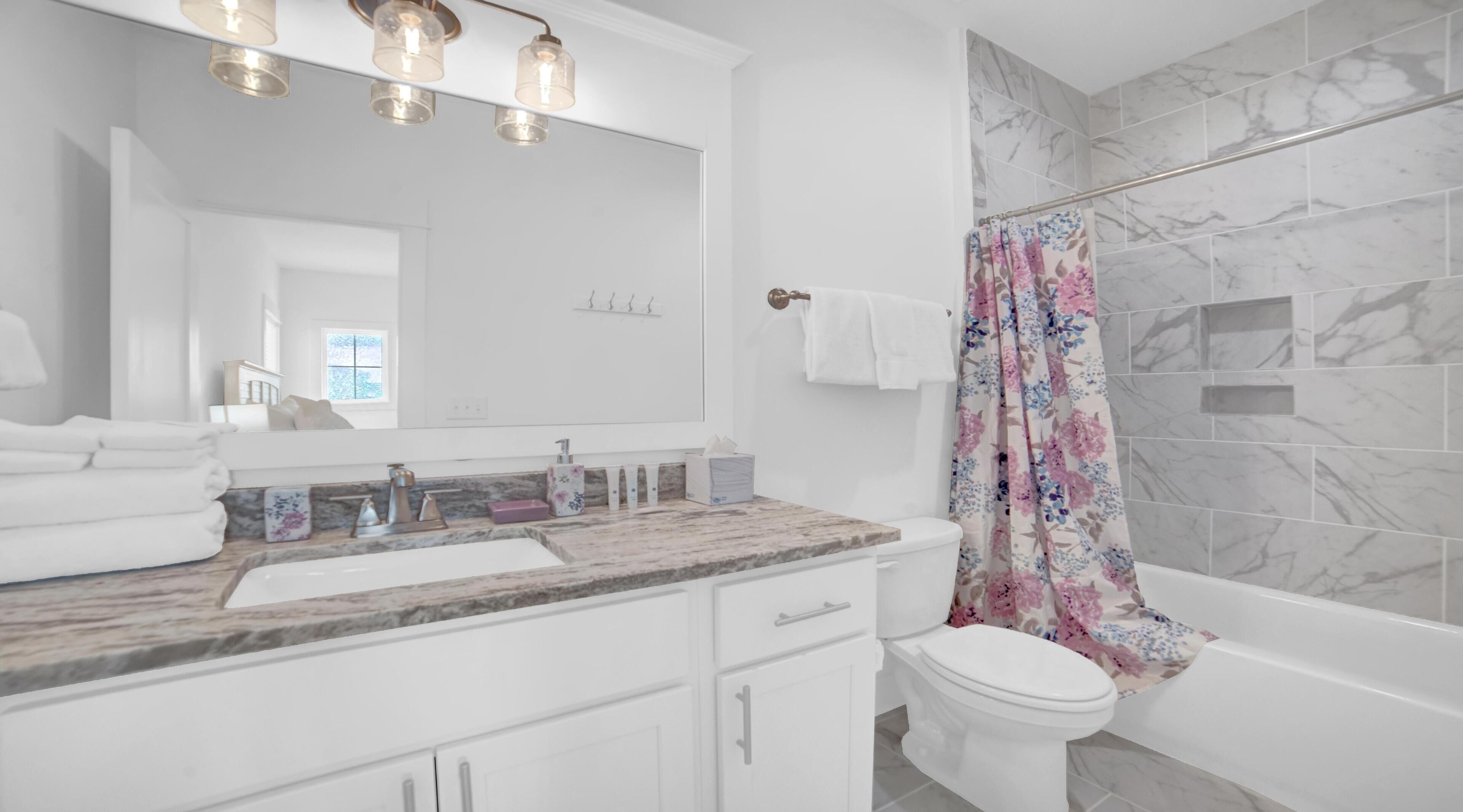 A modern bathroom with a marble sink, a large mirror, and a shower with a floral curtain.