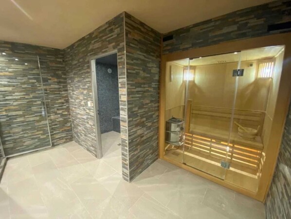 A modern elevator with a glass door and a metal frame, surrounded by textured stone walls and a tiled floor.